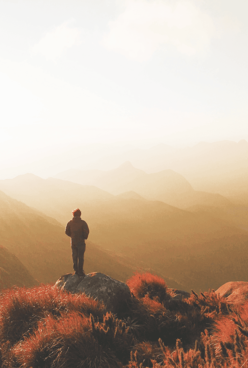 Back of a man walking through a hiking path with silhouettes of mountains in the background. I like mountains because they offer great insights about life in general. Like: we're never quite sure of how tall are the mountains just over the ones that are nearest to us, all we have to do is keep climbing and taking care of our own pair of legs.